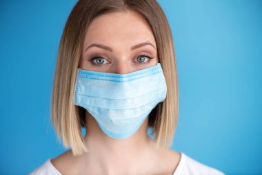 Yüz maskeli hemşire ya da doktor. Sağlık hizmeti, ameliyat. Mavi arka planda beyaz kadın modelinin yakın portresi.