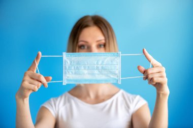 Doktor ya da hemşire mavi arka planda yakın plan yüz maskesi tutuyor. Virüsün yayılmasını önlemek için sağlık ve tıbbi konsept 