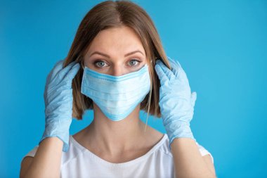 Yüz maskesi ve eldivenleri olan hemşire ya da doktor. Sağlık hizmeti, ameliyat. Mavi arka planda beyaz kadın modelinin yakın portresi.