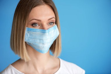 Yüz maskeli hemşire ya da doktor. Sağlık hizmeti, ameliyat. Mavi arka planda beyaz kadın modelinin yakın portresi.