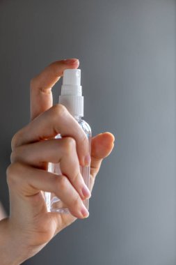 Kadın ya da kız, ellerinde dezenfekte edici sprey alkol ile ellerini dezenfekte ederek gri arka planda virüs bakterilerinin sağlığını önlemeye çalışıyor.