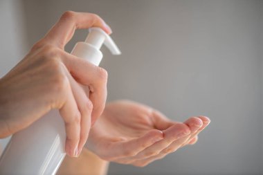 Kadın ya da kız, elinde sabun dezenfektanı olan bir kadın ya da kız, gri arka planda virüs bakterisi önleme çalışmalarına karşı elleri dezenfekte ediyor.