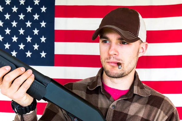 Joven sosteniendo pistola en fondo de bandera americana —  Fotos de Stock