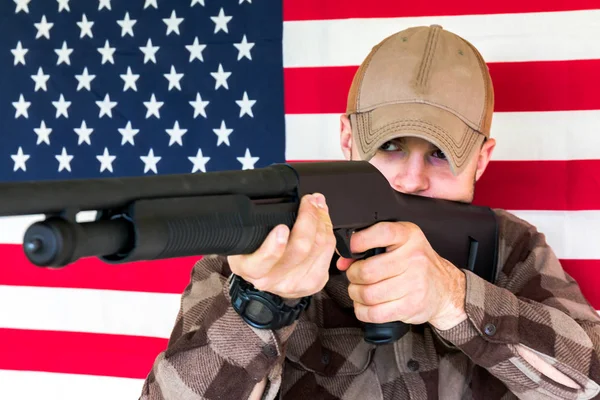 Joven sosteniendo pistola en fondo de bandera americana —  Fotos de Stock