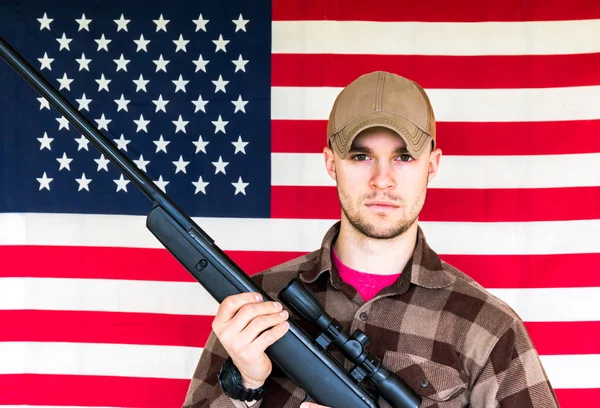 アメリカの国旗の背景に銃を保持している若い男 — ストック写真