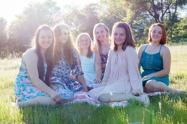 女孩子一起坐在绿草如茵的球场上阳光开销 — 图库照片
