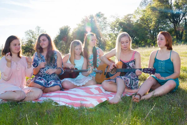 Chicas sentadas juntas en el campo de hierba cantando y tocando música —  Fotos de Stock