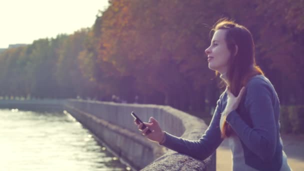 Приваблива молода жінка насолоджується сонцем у парку, коли вона розмовляє по телефону . — стокове відео