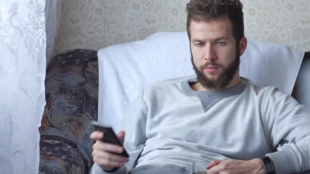 Młody mężczyzna rozmowa na telefon i picie kawy na fotel w domu — Wideo stockowe