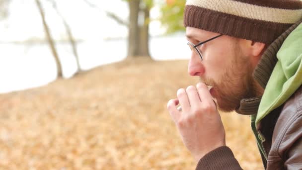 One bearded man lights a cigarette on a bench in autumn park. Thoughtful serious kind of symbolizes sorrow — Stock Video