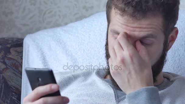 Egy fehér fiatal barna göndör szakállas ember használ a telefon ülő-ban ivás, tea vagy kávé resle — Stock videók