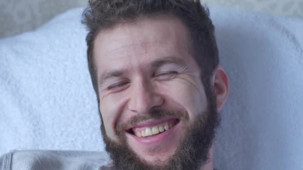 Yavaş çekimde bir sandalyede oturan gülüyor gülen bir beyaz genç esmer kıvırcık sakallı yakışıklı adam — Stok video