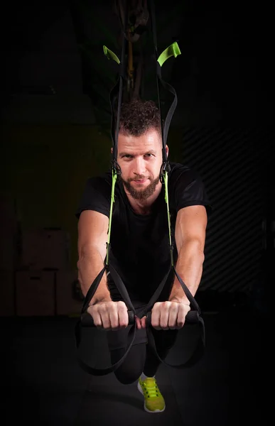 Um jovem bonito bravo encaracolado barbudo musculado homem com uma barba faz Total Resistance eXercises fitness trx tiras trabalhando no ginásio — Fotografia de Stock