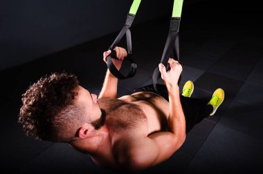 Bir genç yakışıklı cesur kıvırcık sakallı kaslı adam sakallı toplam direnç egzersizleri spor salonunda egzersiz fitness trx askıları yapar.
