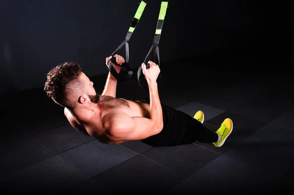 Um jovem bonito bravo encaracolado barbudo musculado homem com uma barba faz Total Resistance eXercises fitness trx tiras trabalhando no ginásio — Fotografia de Stock