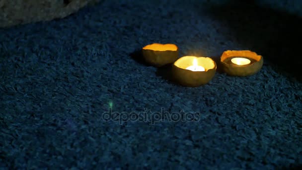 Τρία κεριά σε κηροπήγια πηλό βρίσκονται στο σκοτάδι σχετικά με το σωρό του τάπητα με ένα μεγάλο σκούρο μπλε — Αρχείο Βίντεο