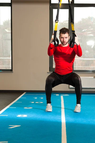 Esportivo masculino exercício com tiras de fitness trx fazendo exercícios o no agachamento no ginásio — Fotografia de Stock