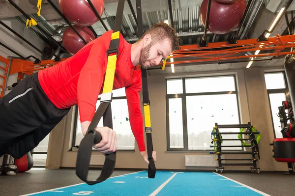 Hvit, krøllete sporty mann som trener med trikkestropper i gymmen – stockfoto