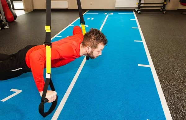 one white curly bearded sporty man exercising push up with fitness straps in gym