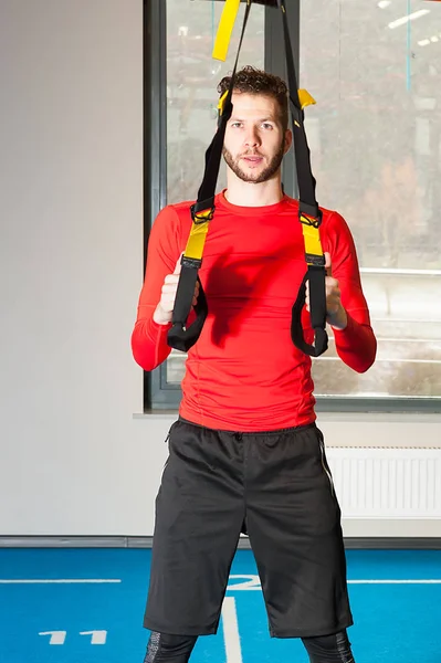 Branco encaracolado barbudo desportivo homem exercitando em pé com alças de fitness no ginásio — Fotografia de Stock