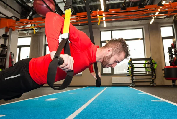 Weißer lockiger, bärtiger, sportlicher Mann, der mit Trageschlaufen im Fitnessstudio trainiert — Stockfoto