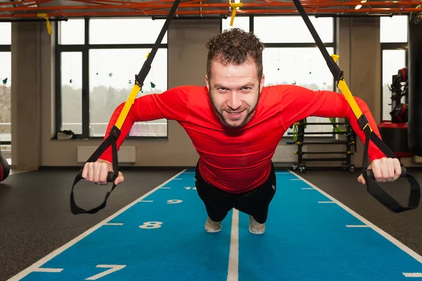 white curly bearded sporty man exercising with trx fitness straps in gym