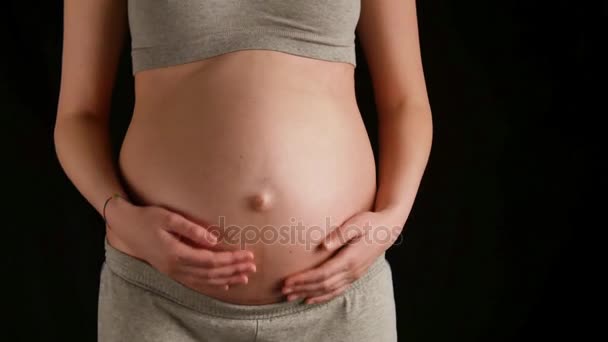Беременная женщина ласкает животик на черном фоне — стоковое видео