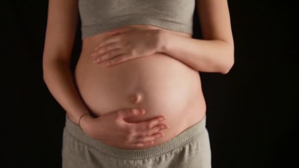 Zwangere vrouw strelen van haar buik op zwarte achtergrond — Stockvideo