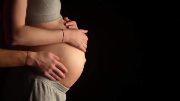 Close-up shot of pregnant woman smoothing the bare belly and future father holding gently his wifes hands. Touching moments of pregnancy black background — Stock Video