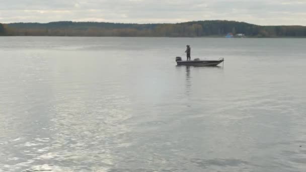 Pescador puxa um peixe viciado no barco no lago. Pescador no barco de pesca no lago — Vídeo de Stock