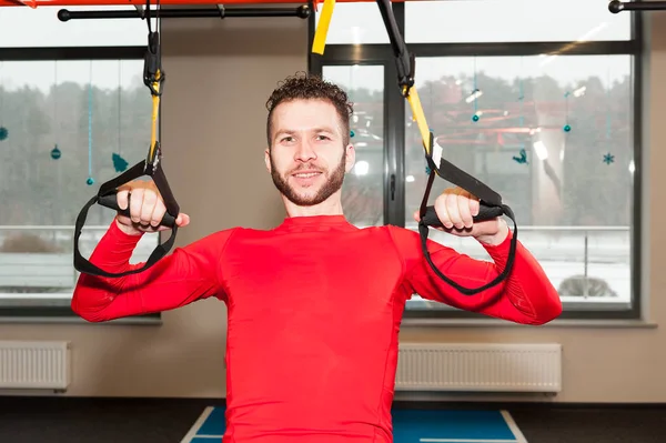 white curly bearded sporty man exercising with fitness straps in gym Crossfit instructor at the gym doing Excersise. Fitness man workout on the rings. Sport and fitness. Crossfit workout
