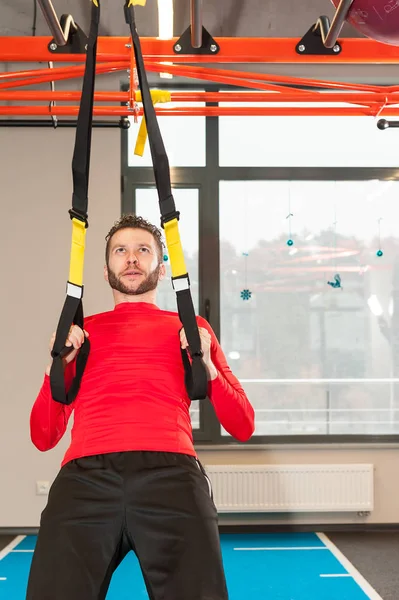 Esportivo masculino exercitando pull-up com tiras de fitness trx no ginásio — Fotografia de Stock