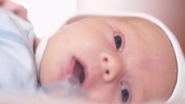 Şirin bir bebek kameraya bakıyor ve beyaz bir çarşaf üzerinde mutlu. Bebek etrafına bakıyor ve sonra gülümsüyor ve gülüyor.