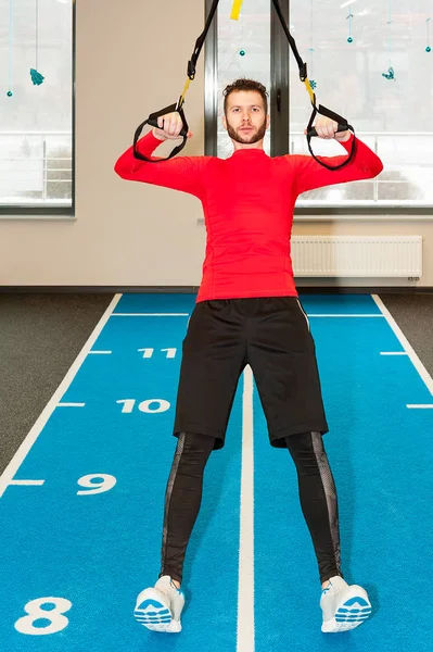 Esportivo masculino exercitando pull-up com alças de fitness no ginásio — Fotografia de Stock
