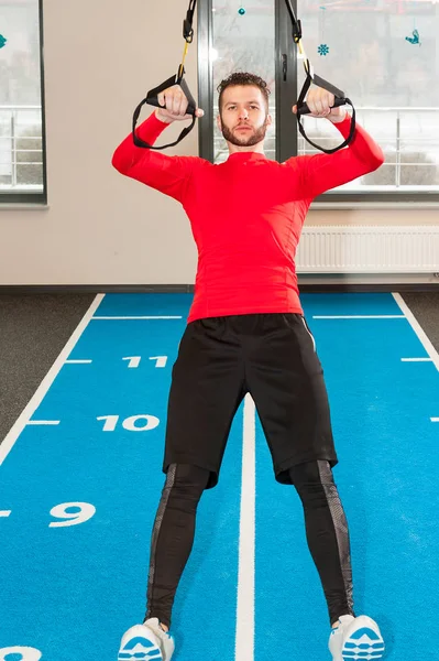Esportivo masculino exercitando pull-up com alças de fitness no ginásio — Fotografia de Stock