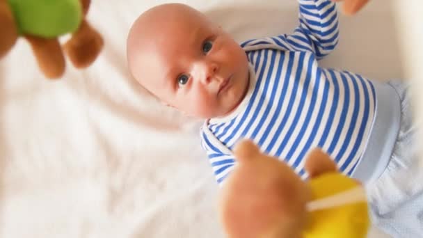 Neugeborener Junge schaut sich Karussell an, Spielzeug dreht sich über Bett — Stockvideo