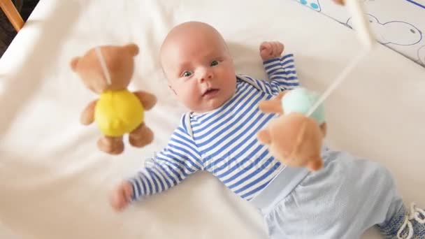 Top view shot of cute baby with soother lying in crib and looking at spinning taddy bear toys — Stock Video