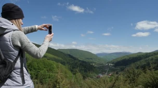 여자는 큰 산의 배경과 녹색 산 강에 대 한 휴대 전화에서 사진이 하고있다. selfie 또는 smartphone에 자화상입니다. 모험과 여행 개념을 즐긴다 — 비디오
