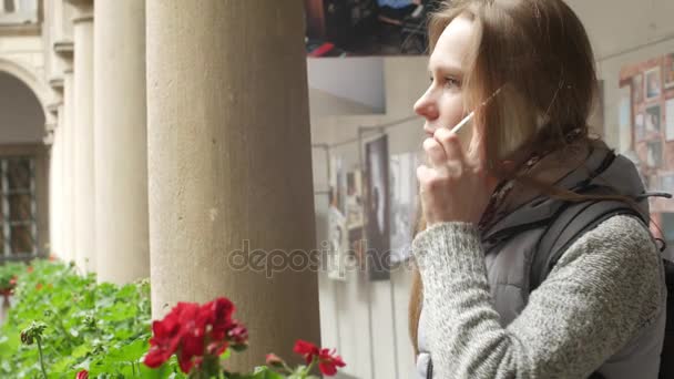 Ελκυστικό λευκό κορίτσι στο μπαλκόνι χρησιμοποιεί ένα κινητό τηλέφωνο στο μπαλκόνι. Στο βάθος όμορφες μεσαιωνικές κολώνες — Αρχείο Βίντεο