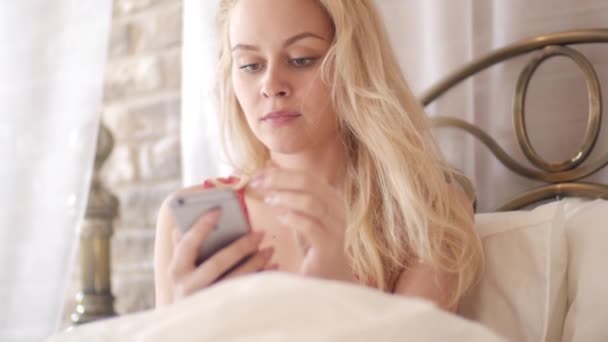 Chica usando el teléfono móvil en la cama - Los dedos hacen gestos tocando texto mecanografiado y deslizando y desplazando la pantalla de un teléfono inteligente moderno — Vídeos de Stock