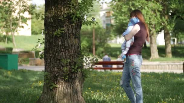 Mamá le muestra al bebé una flor de diente de león. El niño está muy sorprendido y feliz. Un lindo bebé está mirando a la cámara. El bebé mira a su alrededor y luego sonríe y ríe. Concepto de cuidado — Vídeo de stock