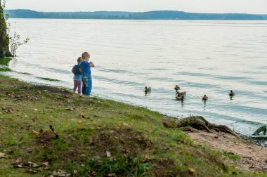 İki sevimli çocuk yaz bir nehir kenarındaki ördek besleme