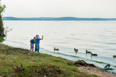 İki sevimli çocuk yaz bir nehir kenarındaki ördek besleme