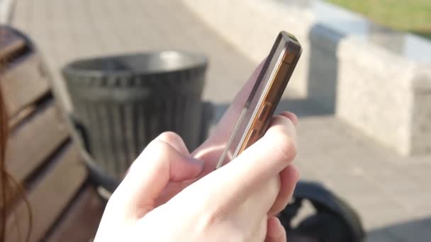 Femme mains à l'aide d'un smartphone à l'extérieur, assis sur le banc dans le parc — Video