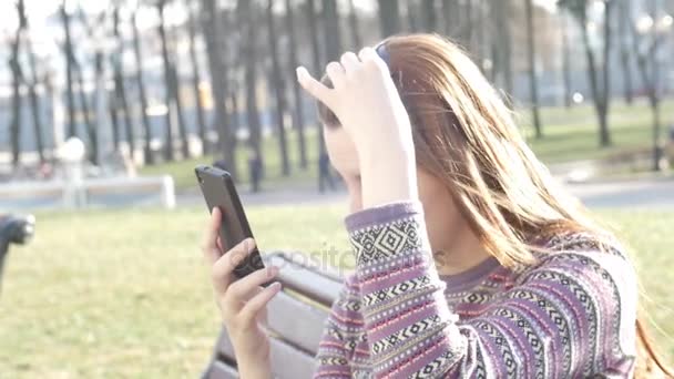 Girl makes selfie outside, sitting on bench in park — Stock Video