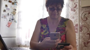 Kredi kartı ve cep telefonu kullanarak gözlüklü yaşlı kadın