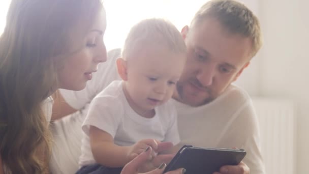 Los padres enseñan al niño a usar un gadget móvil. Los padres jóvenes con un niño usan una tableta . — Vídeos de Stock