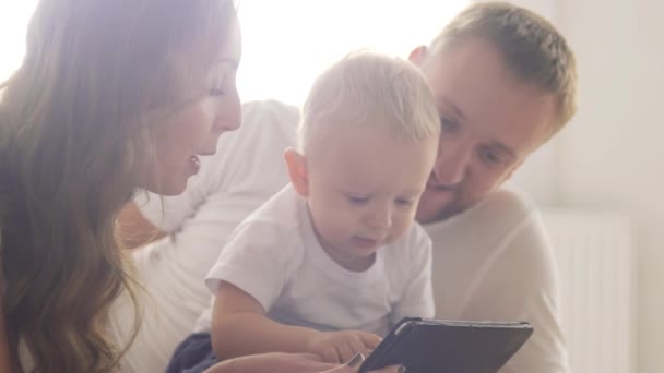 Junge Eltern mit einem Kind nutzen einen Tablet-Computer. Eltern lehren das Kind, ein mobiles Gerät zu benutzen — Stockvideo