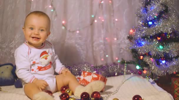 Bebé en pijama de Santa jugar cerca de un árbol de Navidad con un regalo. Concepto de Año Nuevo con niño pequeño — Vídeo de stock