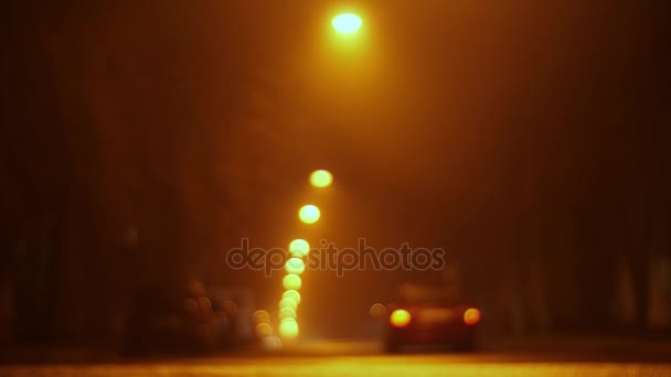 Empty night street in the defocus and fog. lanterns hang over the road, cars drive through and people pedestrians cross the road — Stock Video